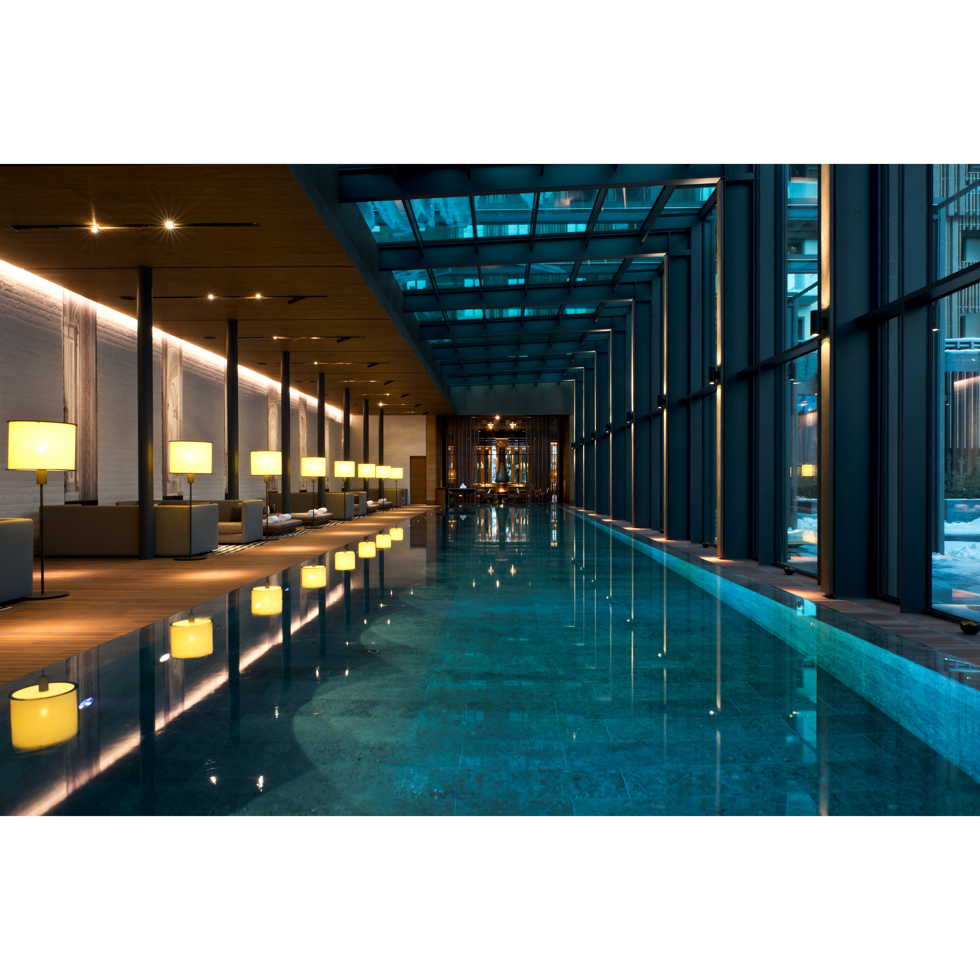 Indoor pool at The Chedi Andermatt. Clear calm water. On the left side are floor lamps next to cozy corners with couches.