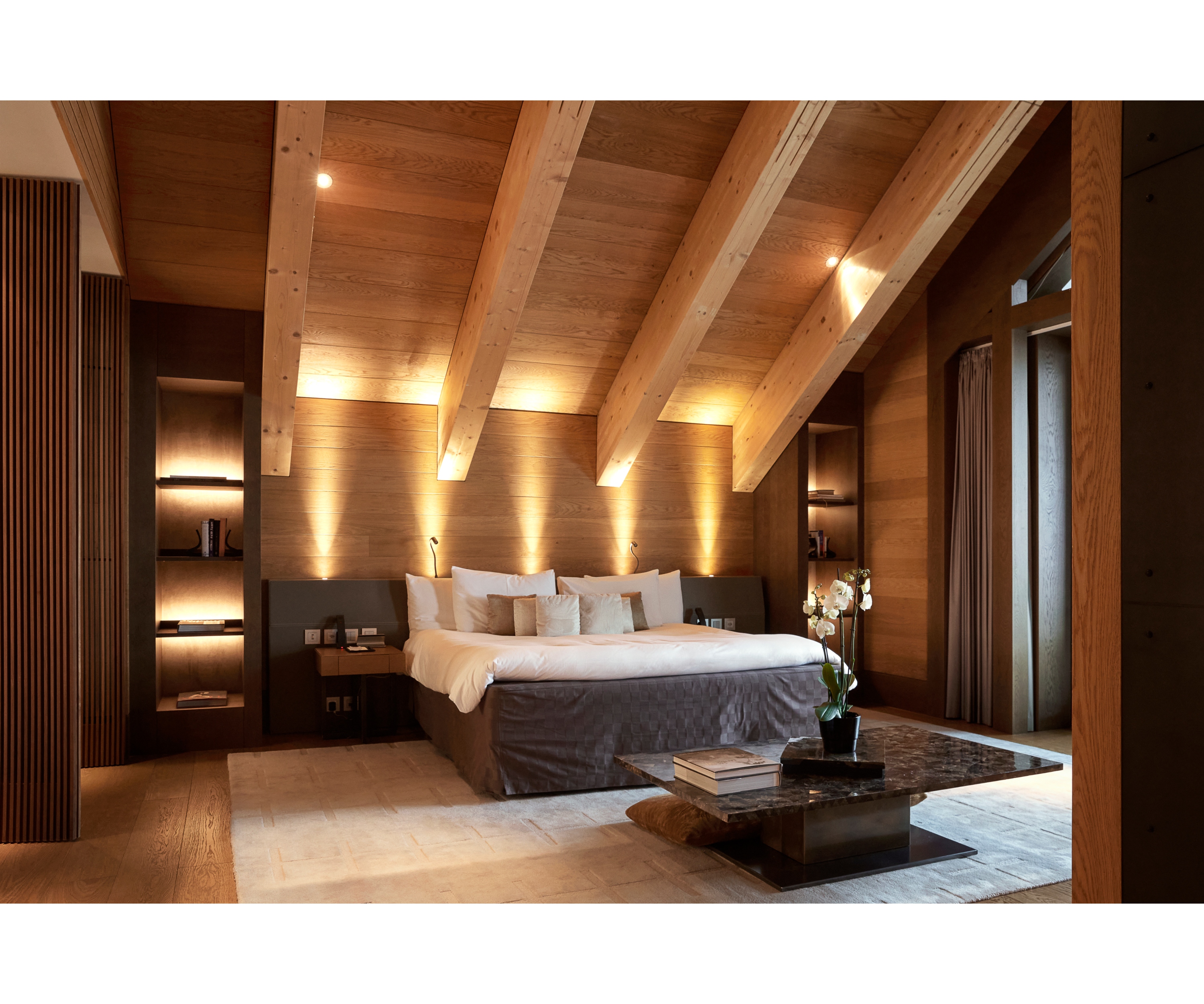 Modernly decorated bedroom at The Chedi Andermatt with generous living space under a high pitched roof with lots of indirect lighting.