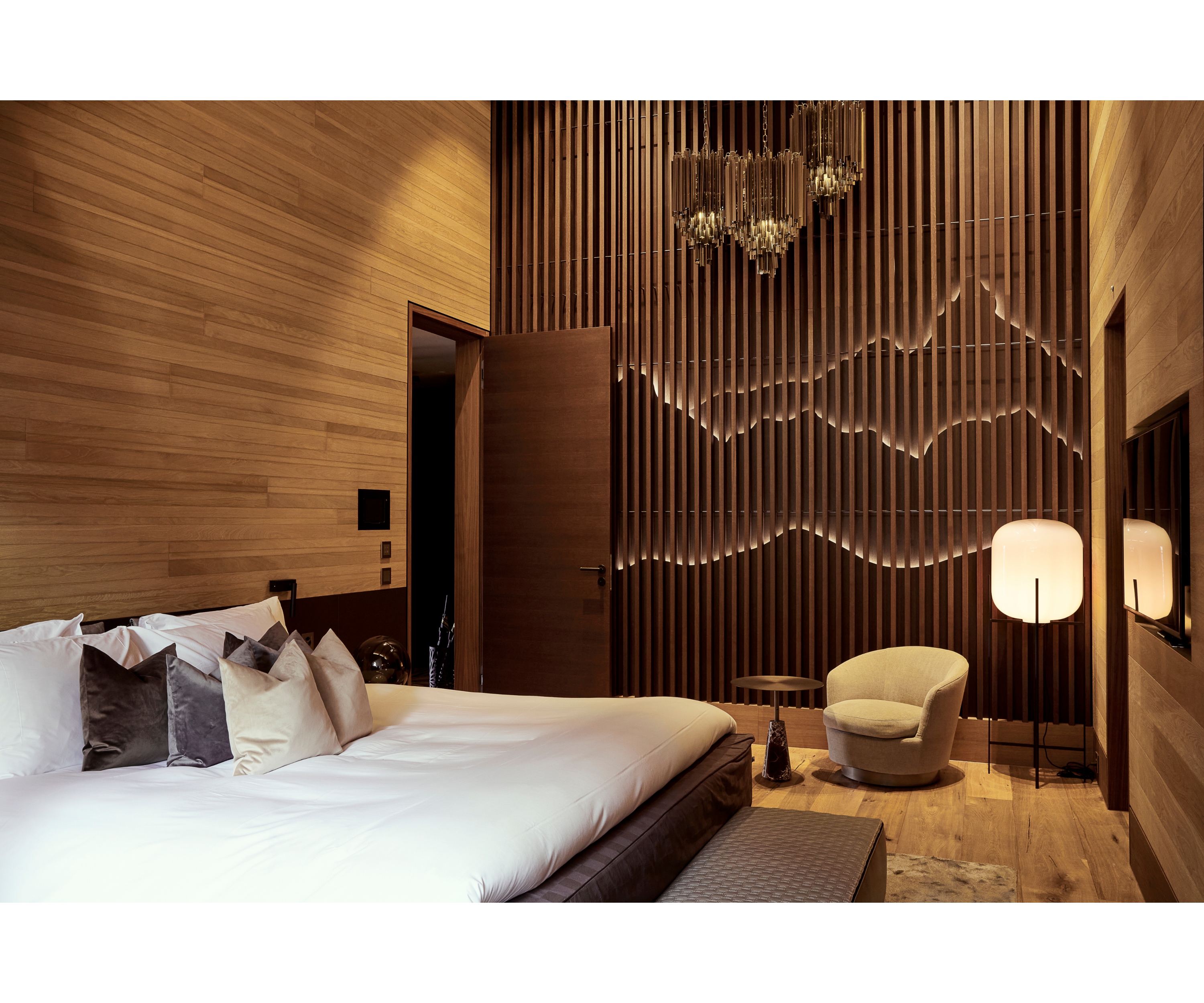 View of a room at The Chedi Andermatt with a wooden slatted wall that lets mountain ranges shimmer through it.