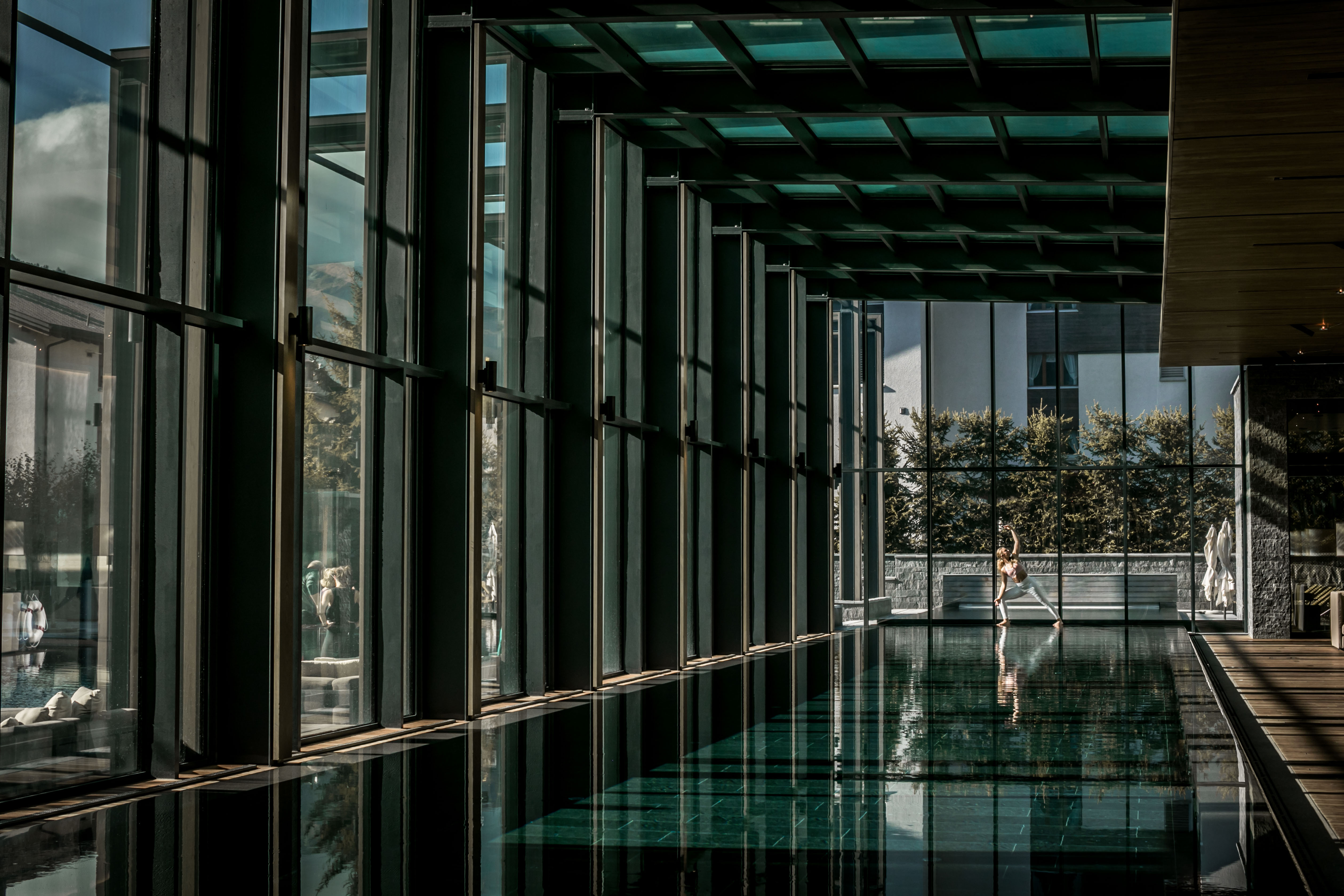 Indoor pool behind a large glass front. At the end of the pool a lady performing yoga exercises. 