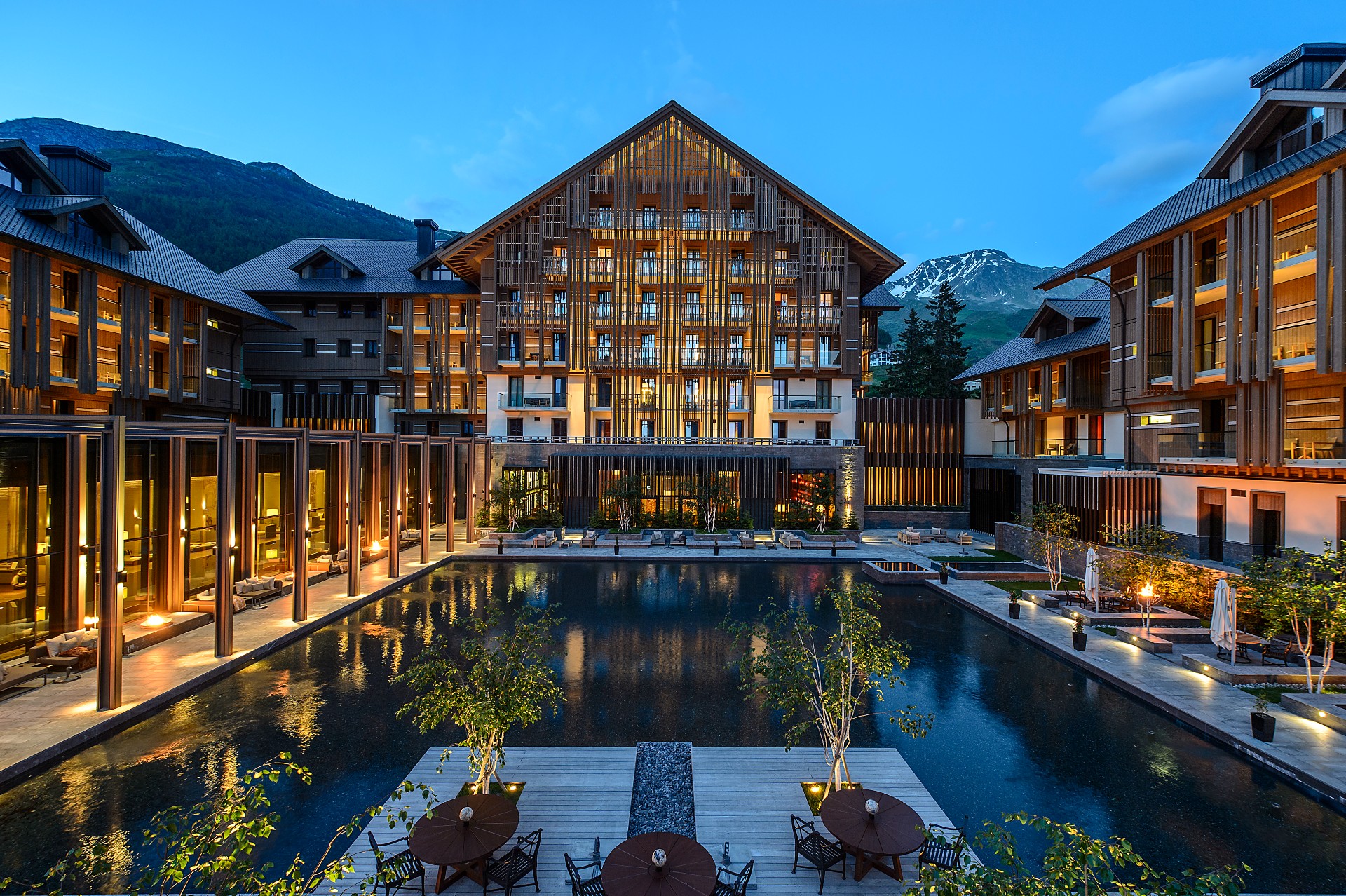 View of The Chedi Andermatt across the outdoor pool. at dusk with illumination of the house.