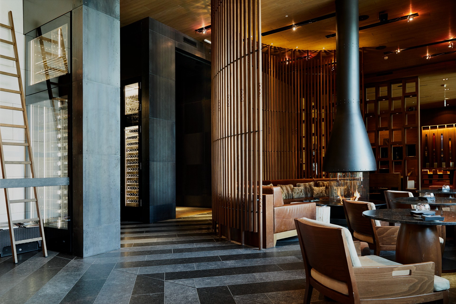Detail of a lounge at The Chedi Andermatt. You can see storage cabinets with wine bottles on the left side and a cozy lounge with fireplace on the right side.
