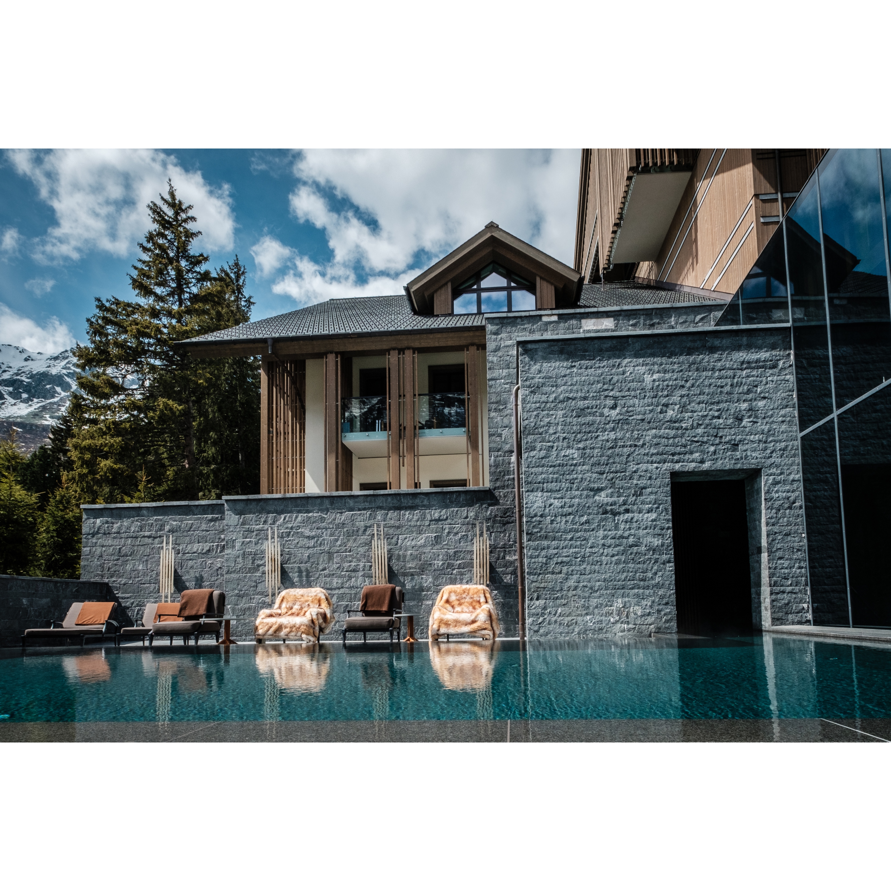 Outdoor pool of at the spa hotel in Switzerland The Chedi Andermatt. With its entrance and sunbeds placed in the sun.